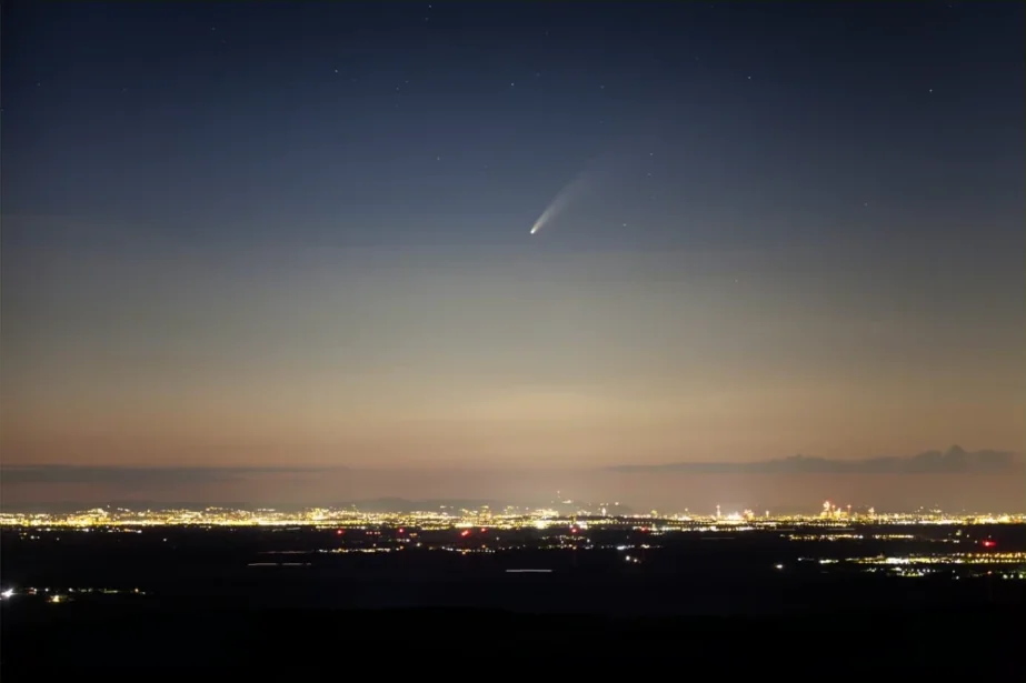 Komet Neowise am Abendhimmel über der Lichterkulisse von Wien